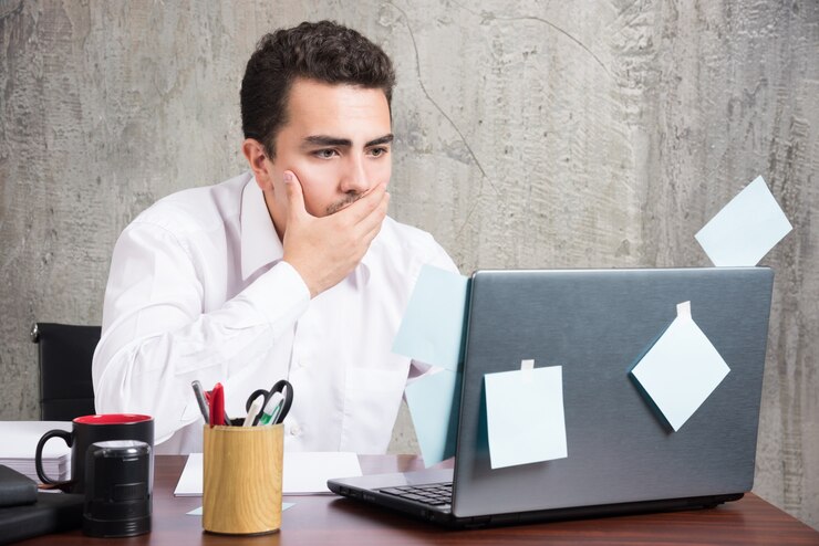 businessman-looking-laptop-while-holding-his-mouth-office-desk_114579-28342